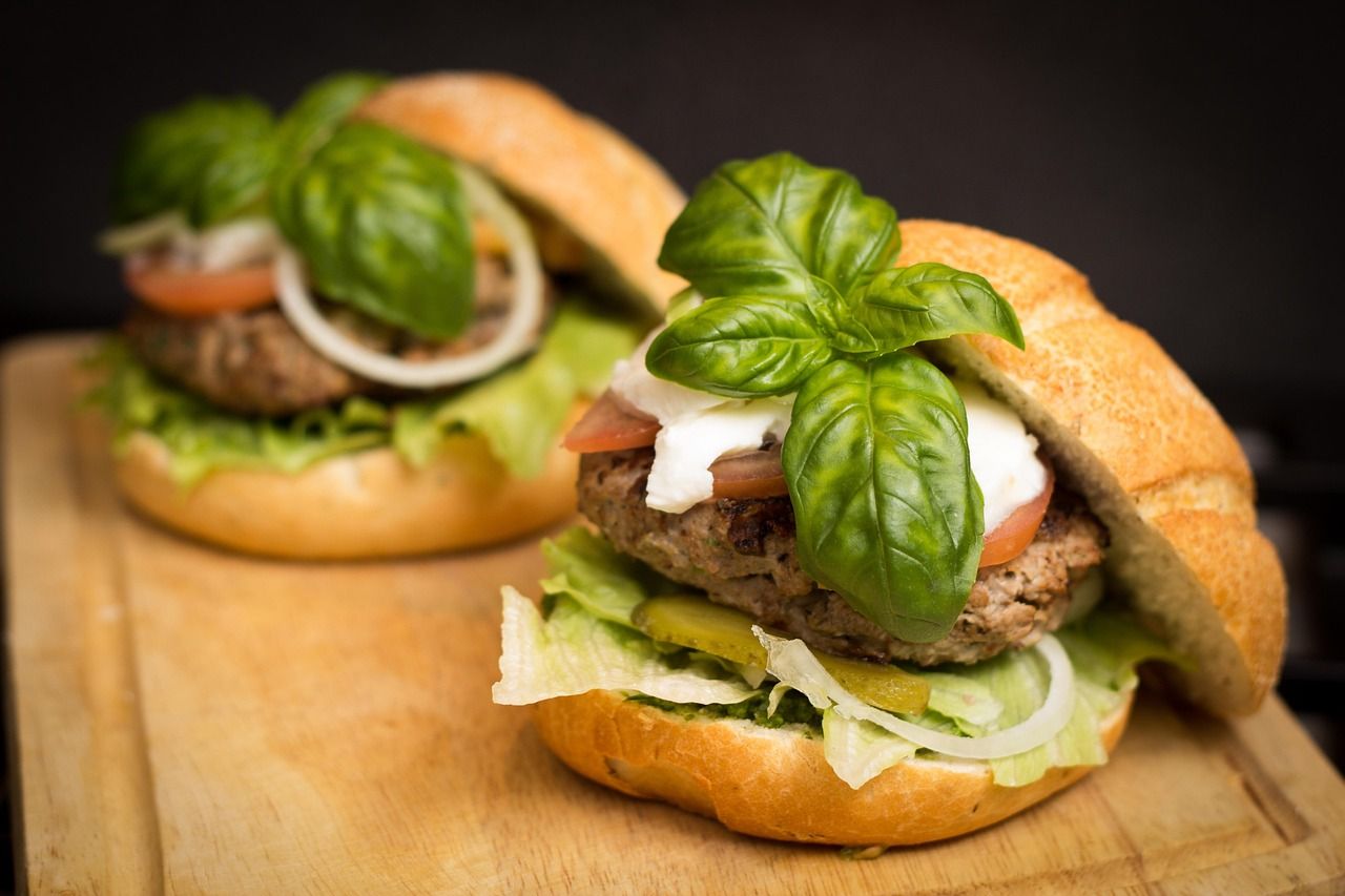 Photo d'illustration : hamburgers garnis de basilic, de tomate et de fromage sur une planche
