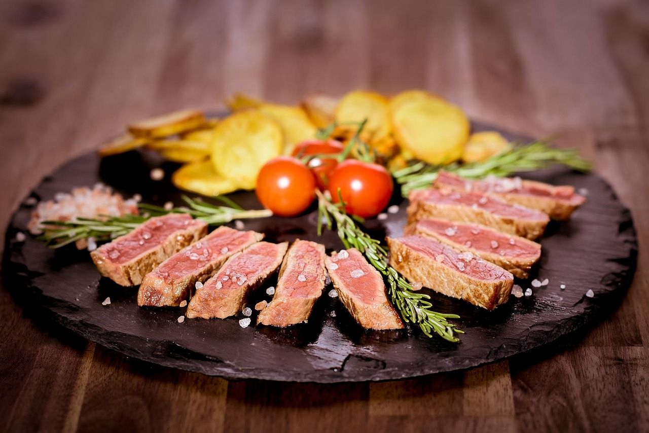 Photo d'illustration : tranches de bœuf rosé sur ardoise, tomates cerises, romarin et pommes de terre